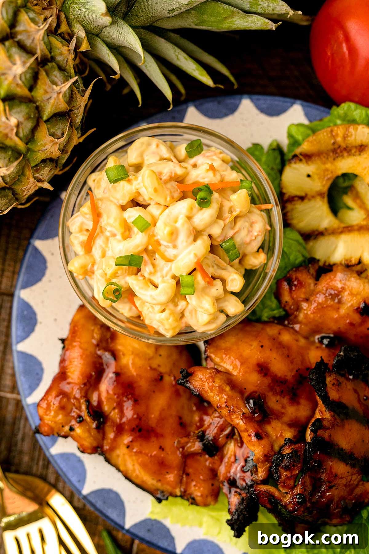 Hawaiian-Style BBQ Chicken with Pineapple Glaze 8 A plate with Hawaiian BBQ chicken, pineapple slices, and a bowl of macaroni salad garnished with green onions.
