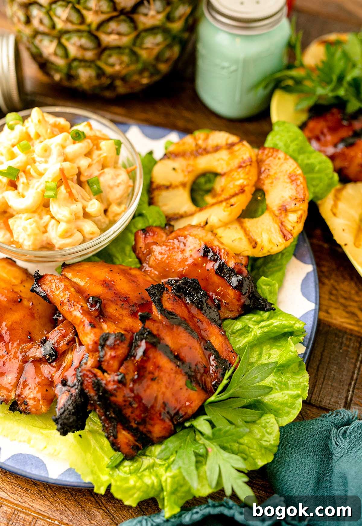Hawaiian-Style BBQ Chicken with Pineapple Glaze 10 Hawaiian BBQ Chicken with glaze, lettuce, grilled pineapple slices, and a bowl of macaroni salad garnished with green onions on a plate.