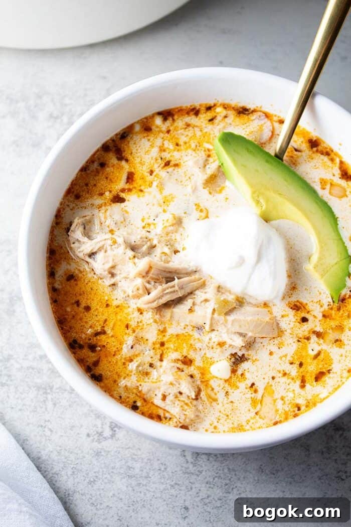 Philly Cheesesteak Keto Lettuce Wraps — Low-Carb Dinner Option 17 overhead view of bowl of keto white chicken chili in white serving bowl and gold serving spoon and garnished with slice of avocado and sour cream