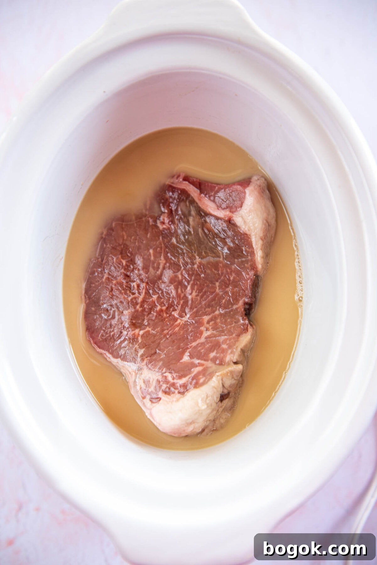 Mississippi Pot Roast Recipe for Tender Slow-Cooker Comfort 5 uncooked 1lb of roast in broth in white slow cooker bowl