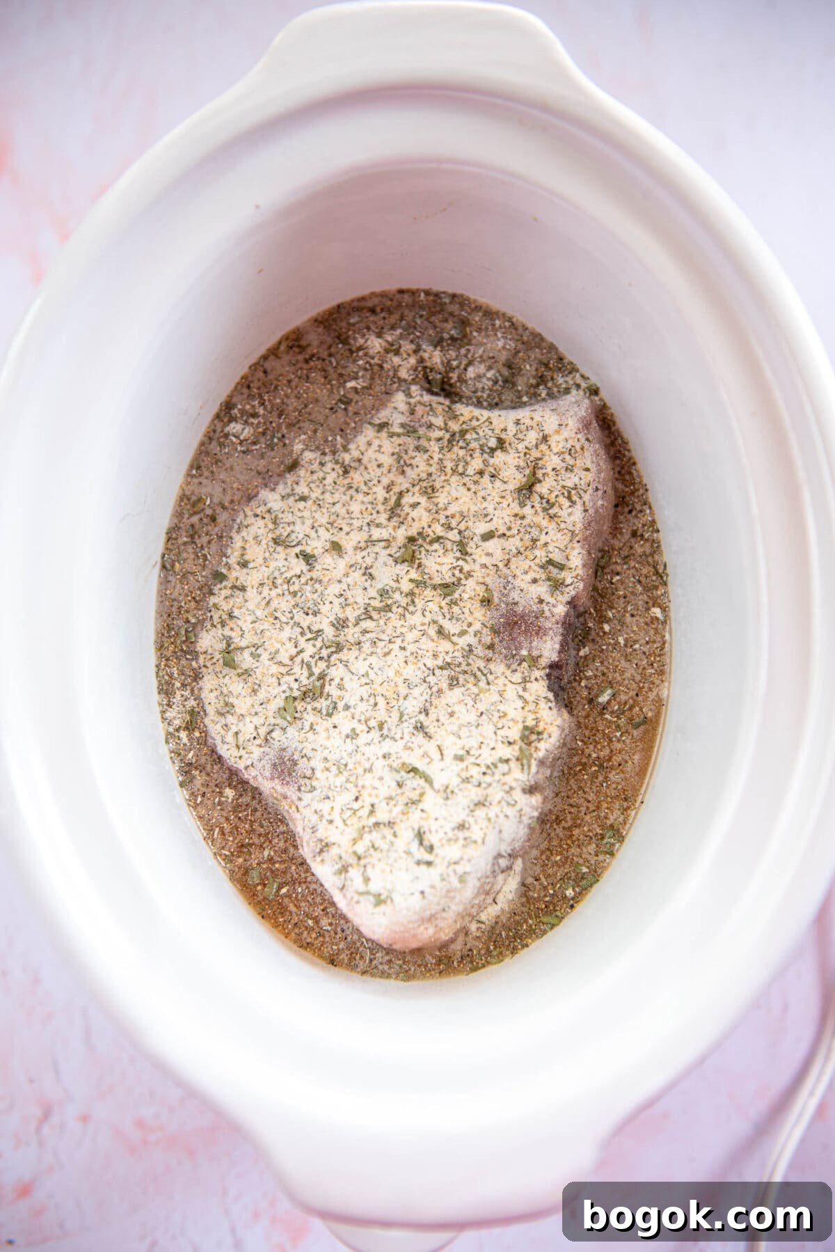 Mississippi Pot Roast Recipe for Tender Slow-Cooker Comfort 8 roast with flour, broth and mixture of spices inside white slow cooker bowl