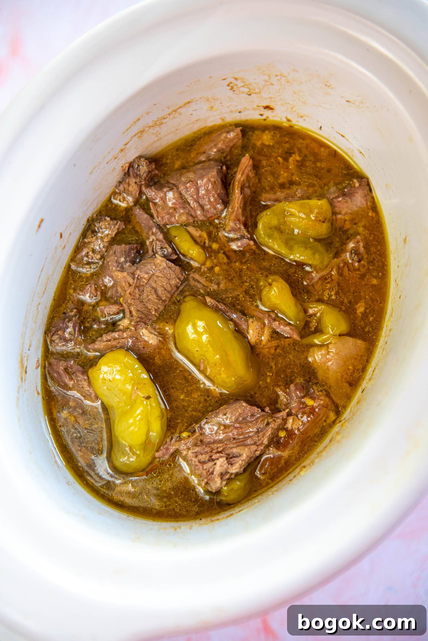 Mississippi Pot Roast Recipe for Tender Slow-Cooker Comfort 10 roast in brown liquid mixture and peperocinis on top inside white slow cooker bowl