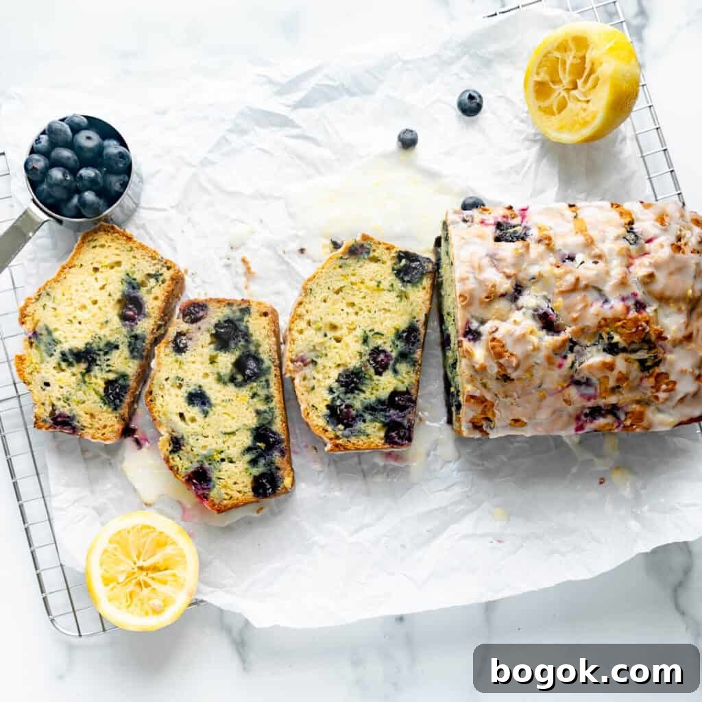 Blueberry Zucchini Bread on white parchment paper with lemon and blueberries around it.
