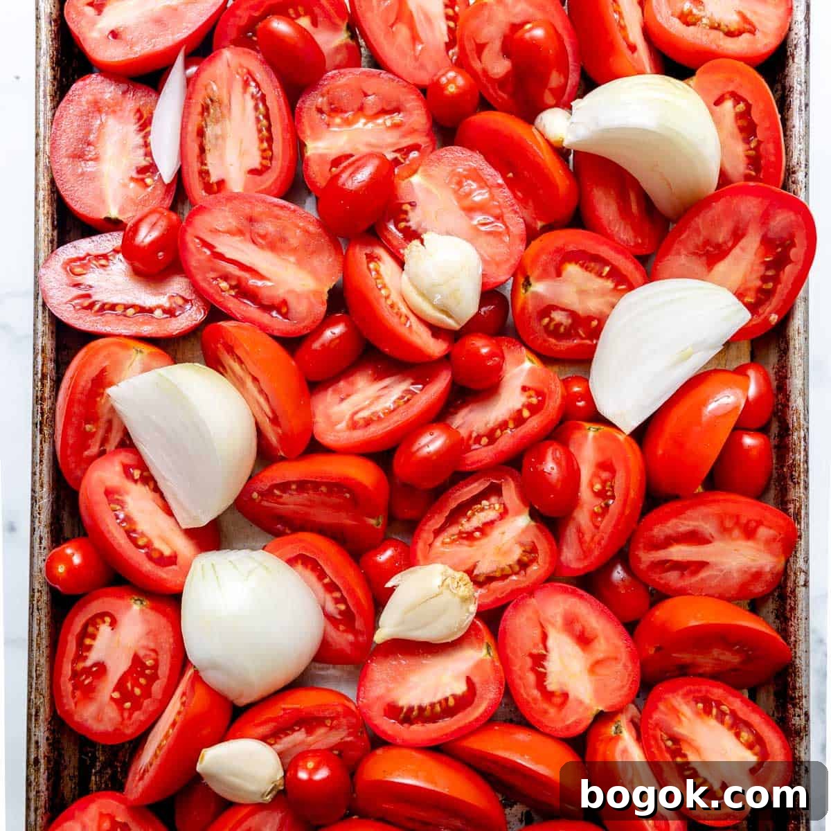 A baking tray filled with halved tomatoes, quartered onions, and whole garlic cloves, ready for roasting.