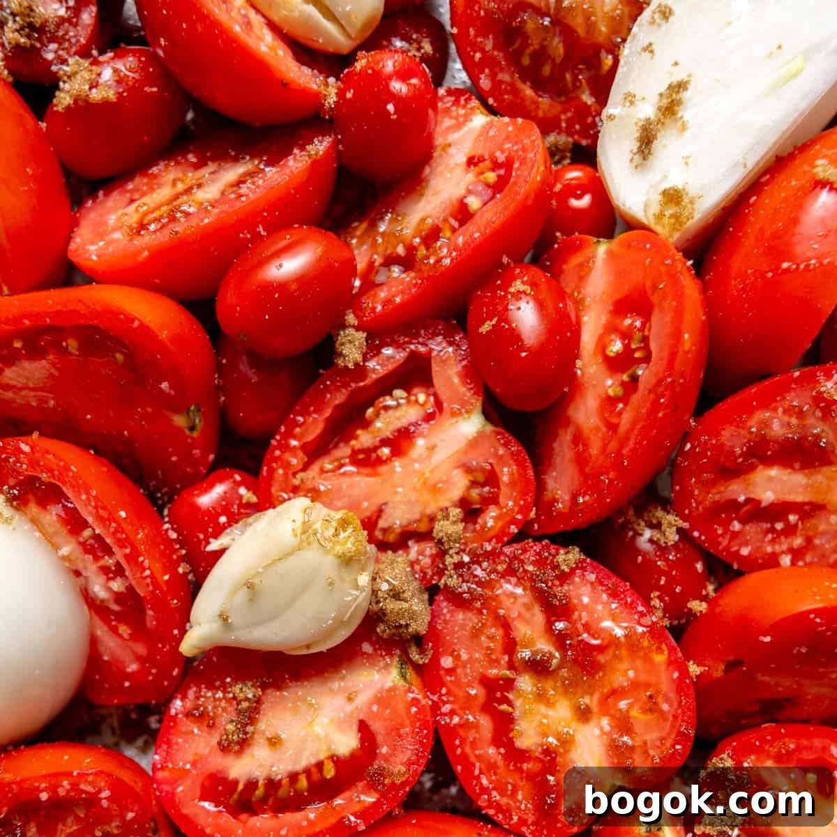 Halved tomatoes, whole cherry tomatoes, garlic cloves, and onion pieces sprinkled with brown sugar on a surface.
