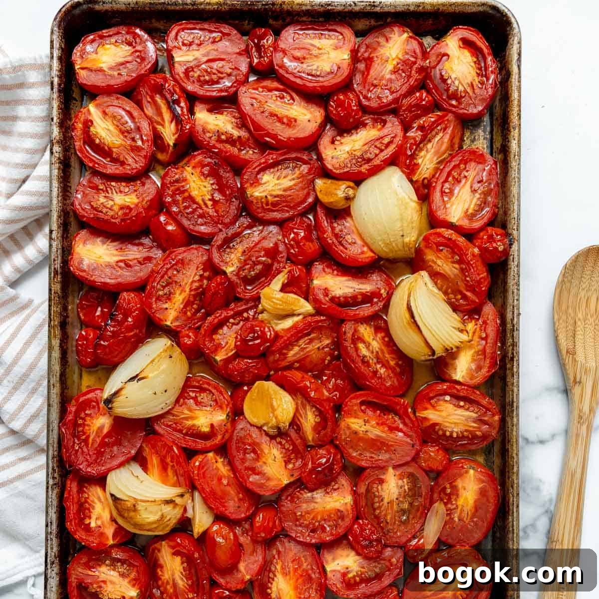 Halved tomatoes, onion wedges, and garlic cloves arranged on a baking sheet, roasted.