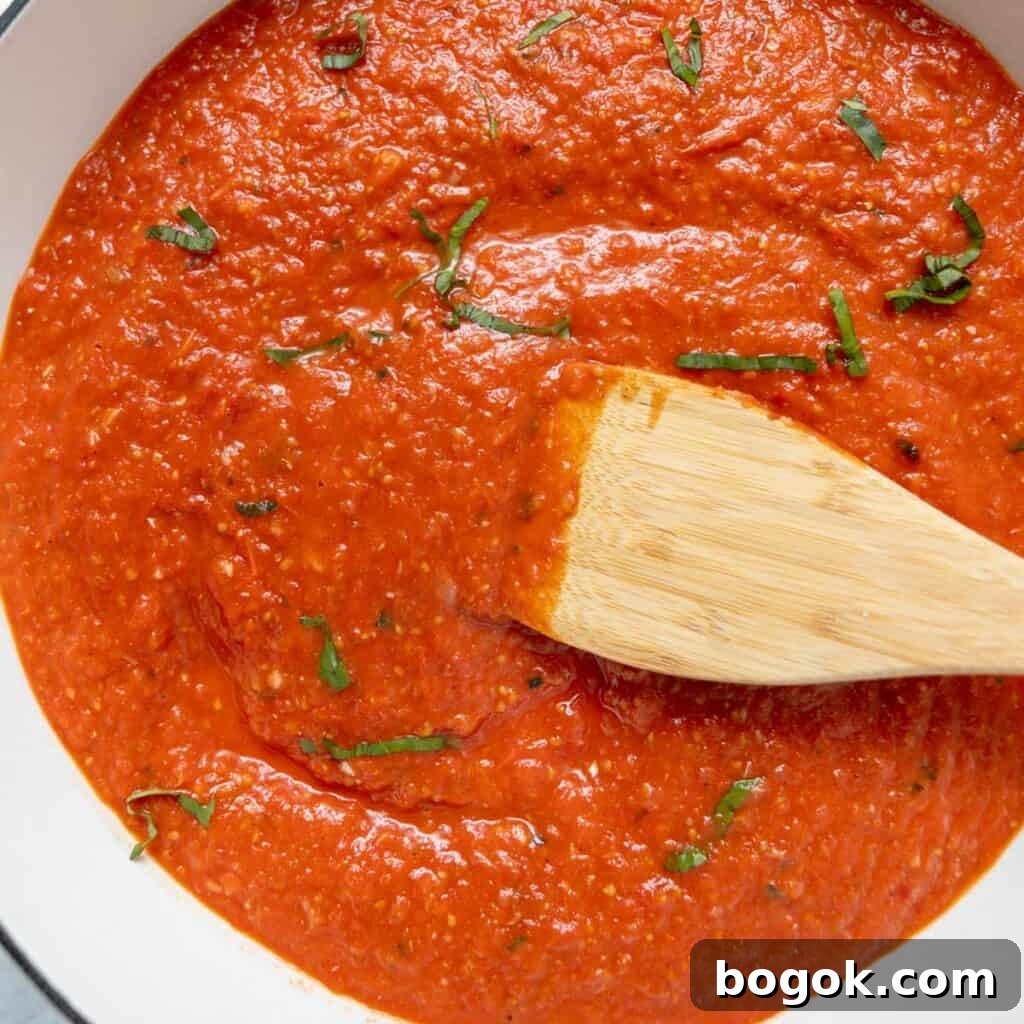 Tomato sauce with chopped basil, stirred with a wooden spatula in a white pot.
