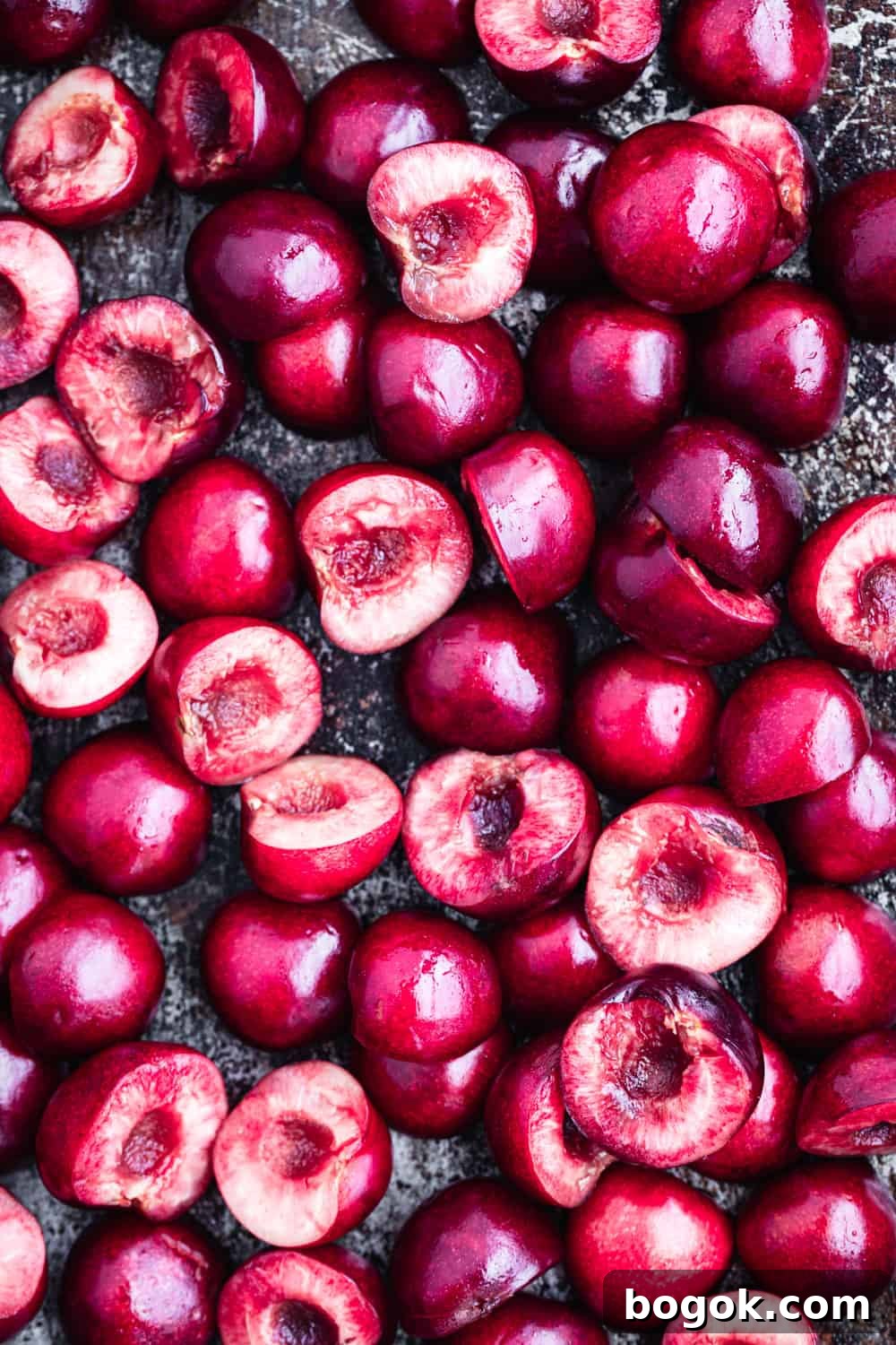 Roasted Cherries in 15 Minutes: Sweet, Syrupy Recipe 3 Overhead close-up of halved and pitted fresh dark red cherries on a dark baking sheet before roasting.