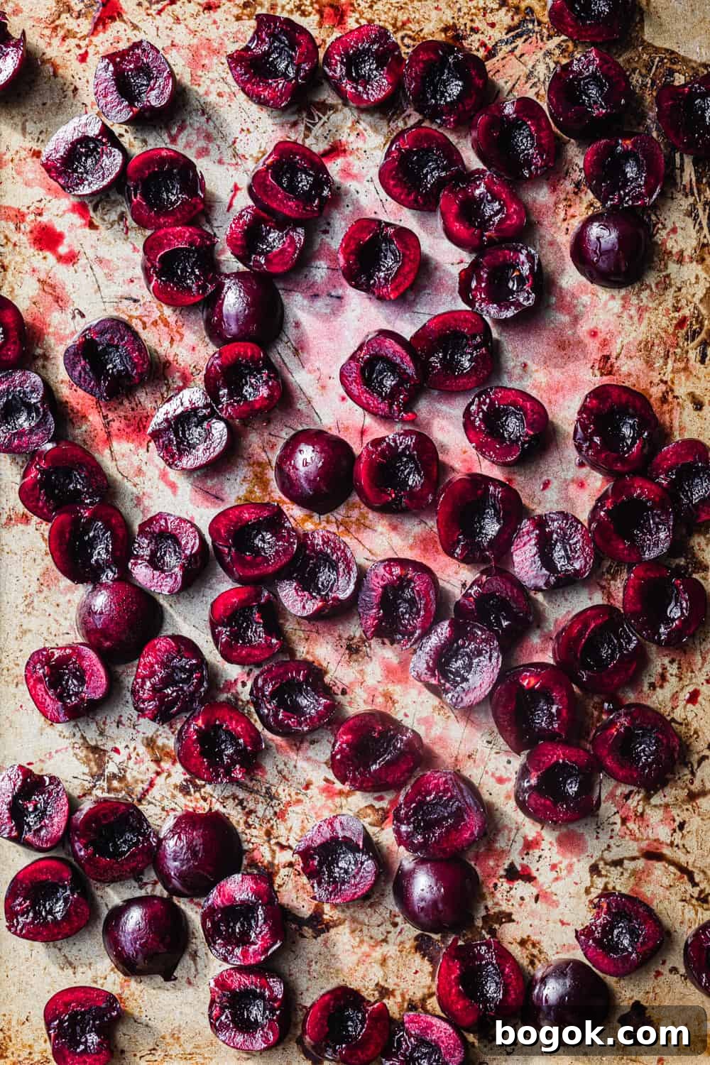 Roasted Cherries in 15 Minutes: Sweet, Syrupy Recipe 5 Raw fresh cherries cut in half on a gold baking sheet, overhead shot.