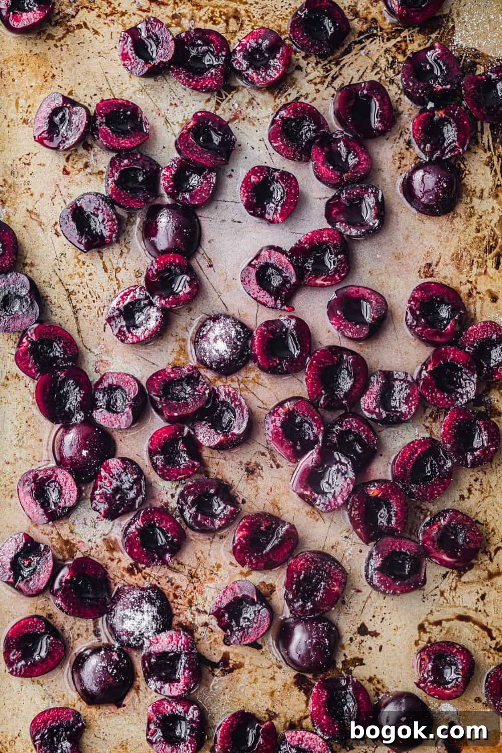 Roasted Cherries in 15 Minutes: Sweet, Syrupy Recipe 6 In process shot of raw fresh cherries sprinkled with sugar on gold baking sheet, overhead shot.
