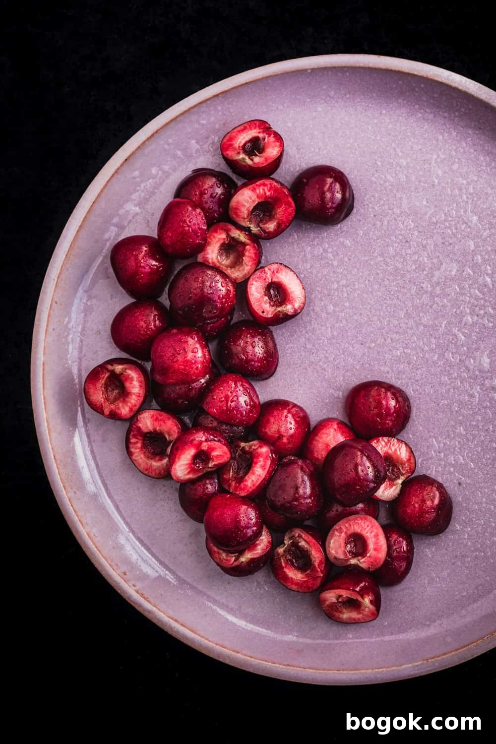 Roasted Cherries in 15 Minutes: Sweet, Syrupy Recipe 8 Pitting cherries, cut in half, on a pink plate, overhead shot.