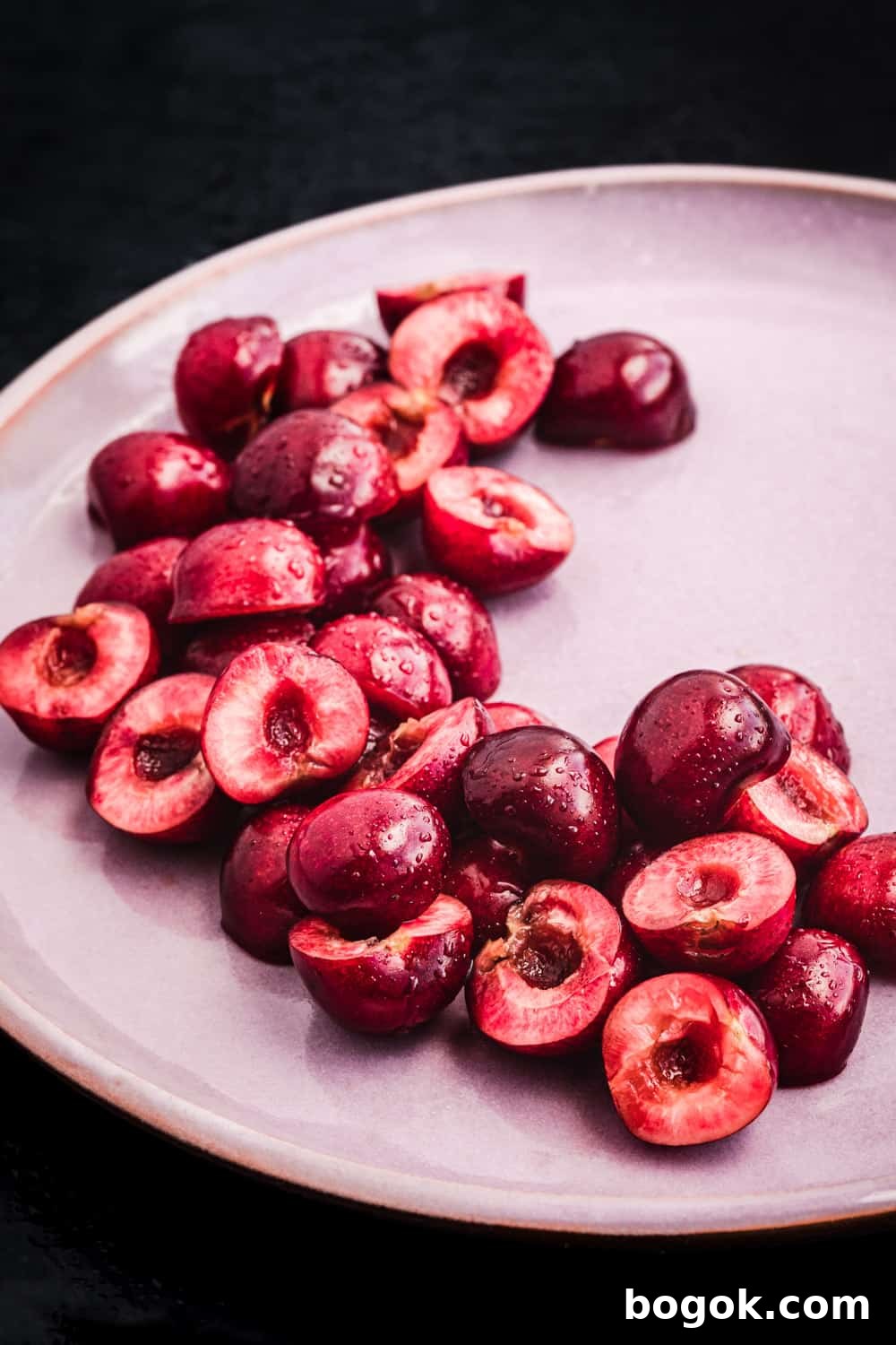 Roasted Cherries in 15 Minutes: Sweet, Syrupy Recipe 10 Pitted cherries, cut in half, on a pink plate, side angle shot.