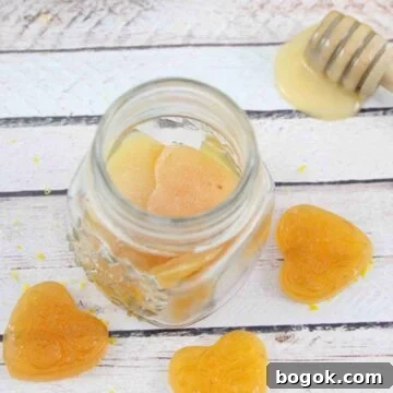 Three honey lemon cough drops around a jar of more cough drops with a honey stick, fresh lemon and a blue linen behind them.