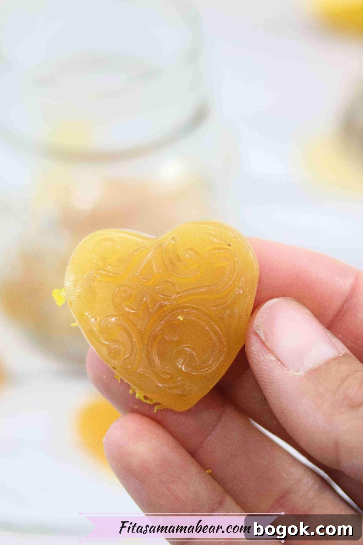 Hand holding a homemade honey lemon cough drop in a heart shape up close.