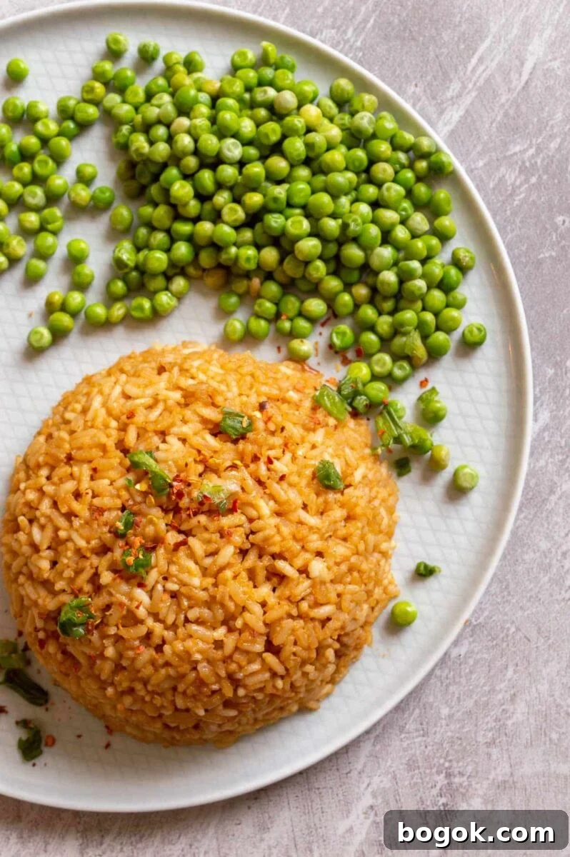 A mound of brown-colored rice on a pale grey plate with green peas.