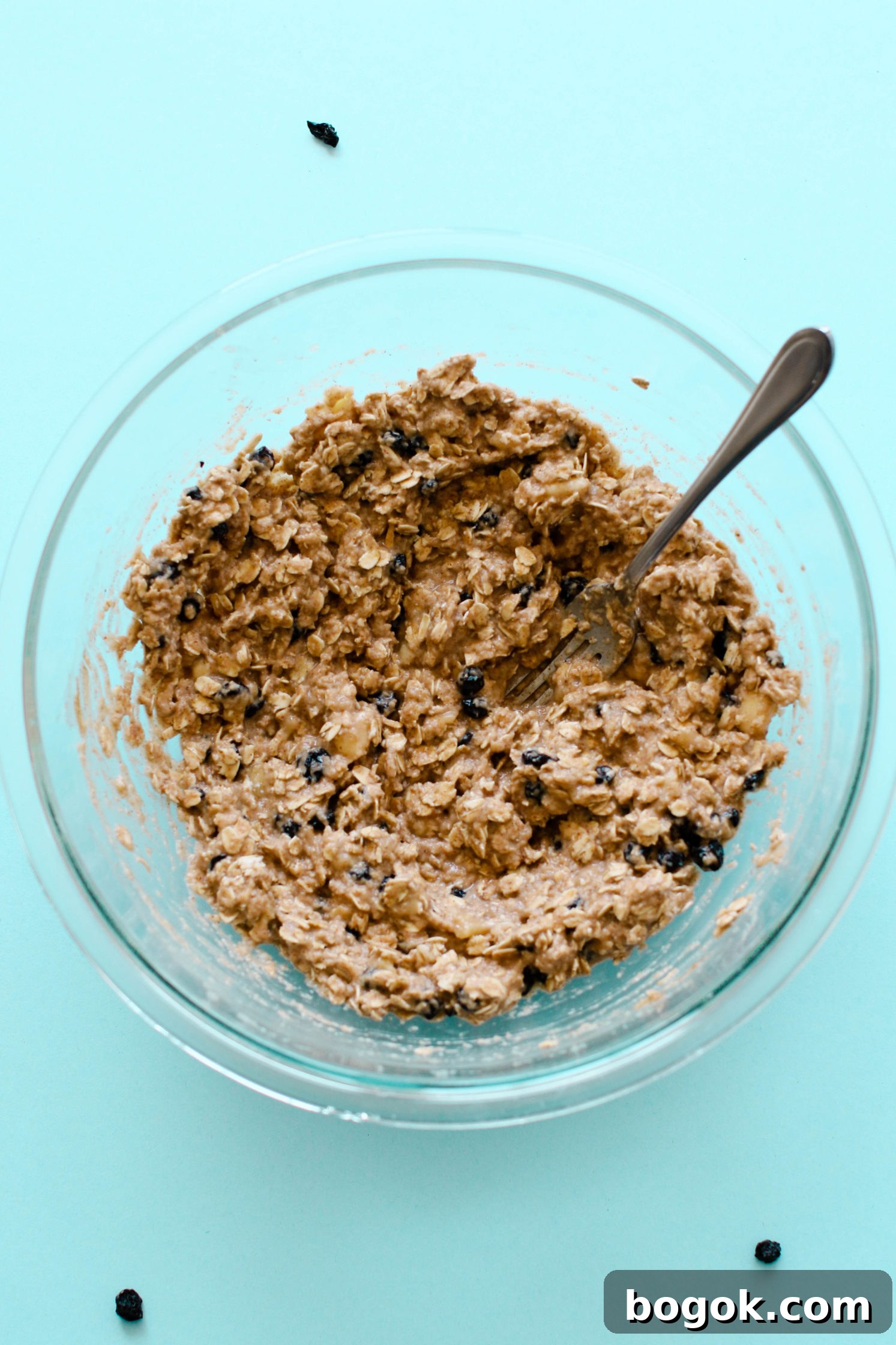 Blueberry Banana Breakfast Cookies batter mixed in glass bowl with fork on blue background