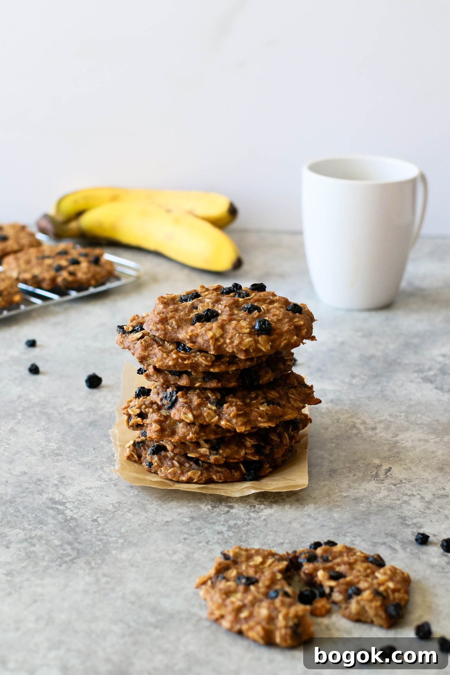 Blueberry Banana Breakfast Cookies stacked on parchment paper with coffee mug and banana in background