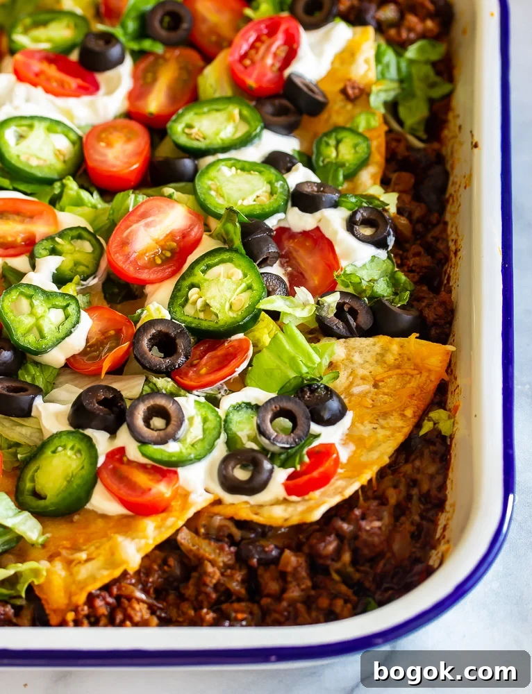 Tortilla Taco Casserole Recipe: Cheesy Mexican Layer Bake 2 A pan with taco seasoned ground beef topped with shredded cheeses and tortilla chips and jalapenos, beans and tomatoes