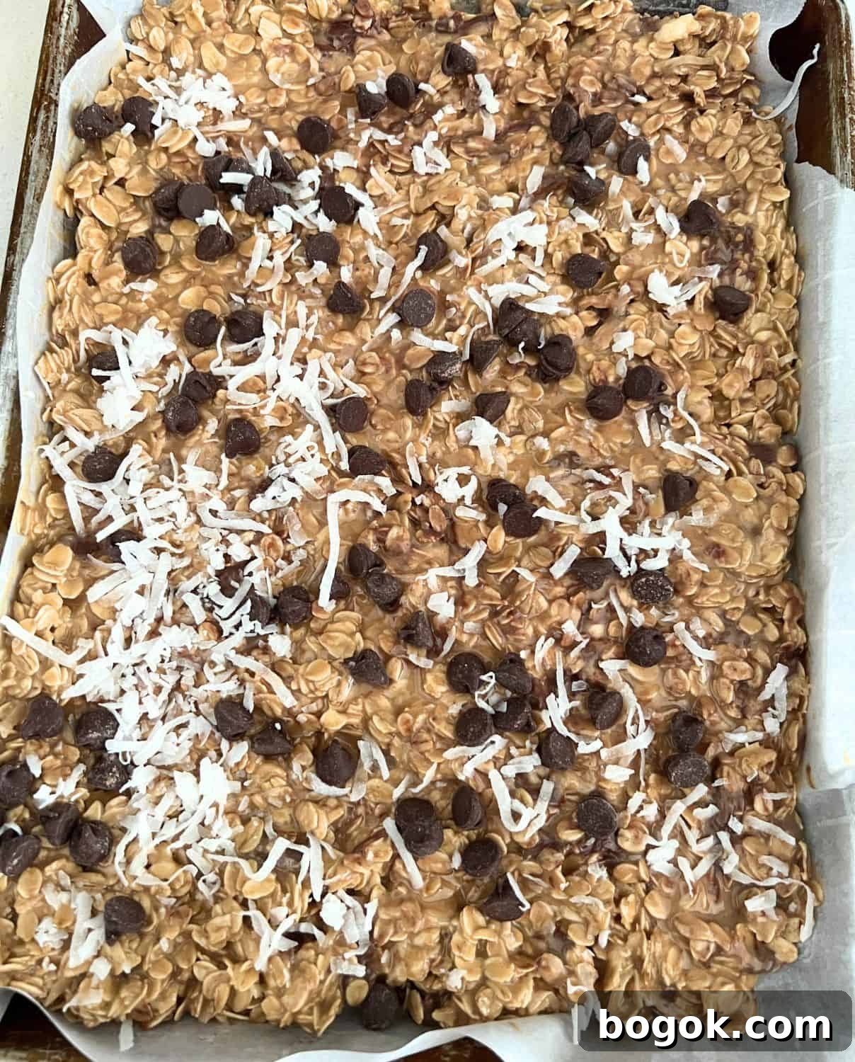 Granola mixture pressed down on a pan and topped with chocolate chips and coconut. 