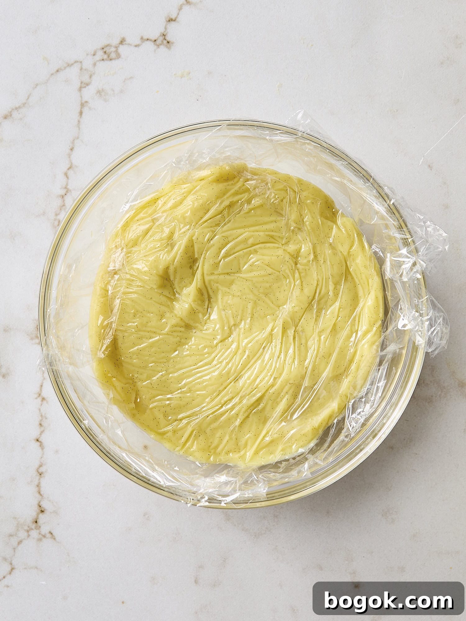 Cooling pastry cream mixture with plastic on top.