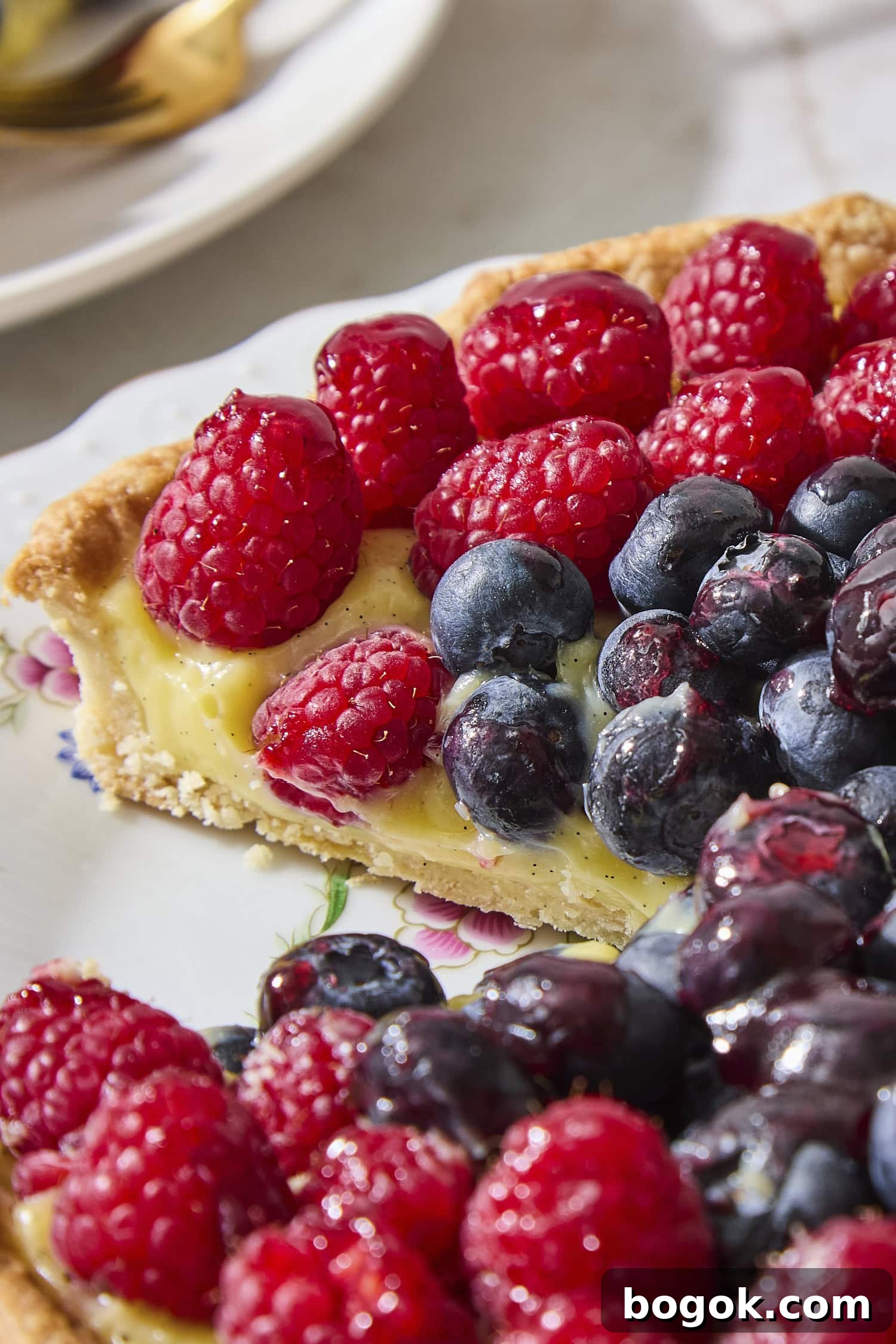 Slice taken out of a fresh fruit tart with pastry cream filling and berries on top.