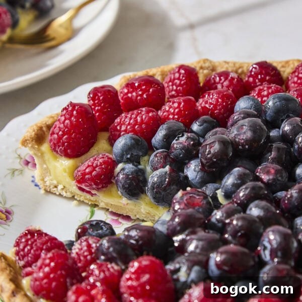 Slice taken out of fruit tart with pastry cream and berries.