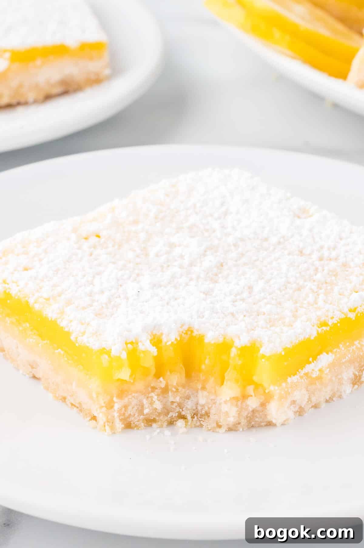 Classic Lemon Bars with Buttery Shortbread Crust 8 The recipe on a plate with a bite out of it.