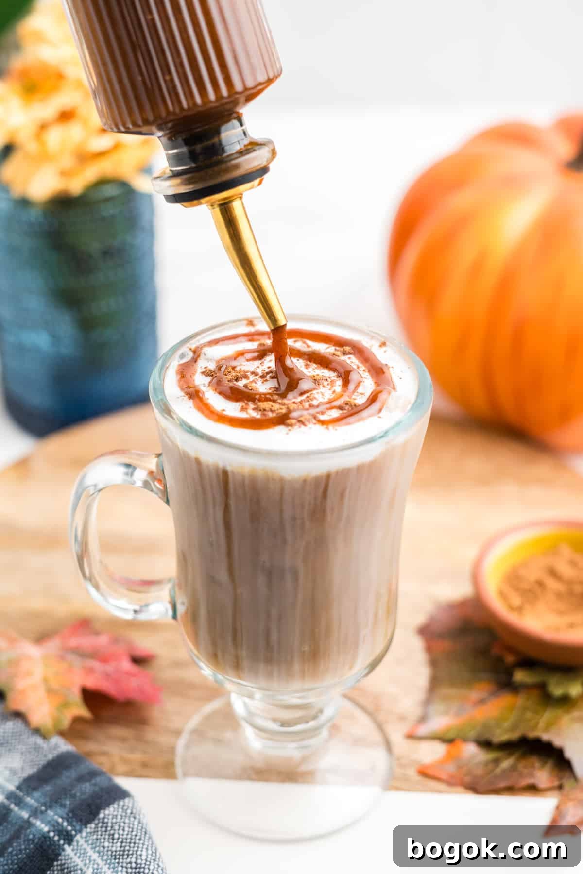 An image of fresh pumpkin spice syrup being poured over iced coffee with a sweet cream foam topping.