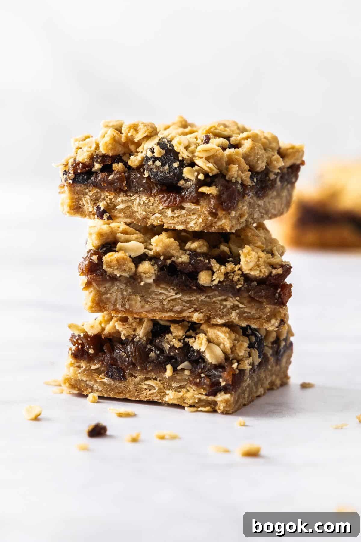 Fruit Mince Oatmeal Bars Recipe — Chewy Fruit & Oat Squares 2 Stack of three pieces of Fruit Mince Oatmeal Bars sitting on a marble benchtop.