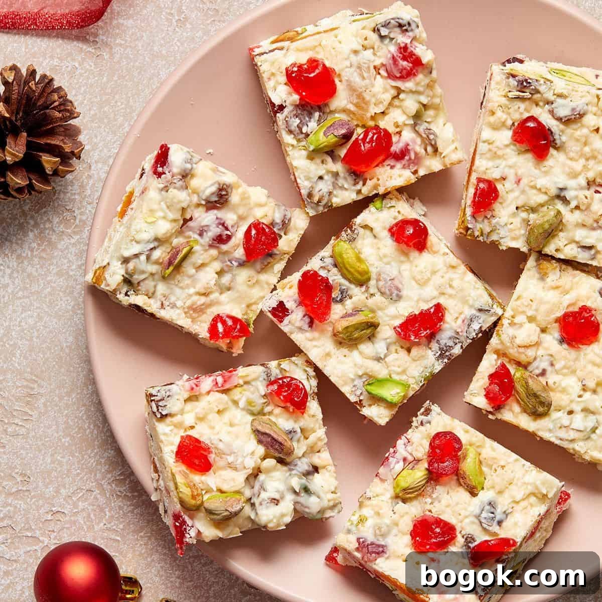 Round pink plate with squares of White Christmas Slice on it, and a couple of Christmas baubles and pine cones around the edge.