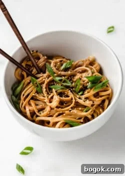 Peanut butter noodles in a white bowl topped with green onions