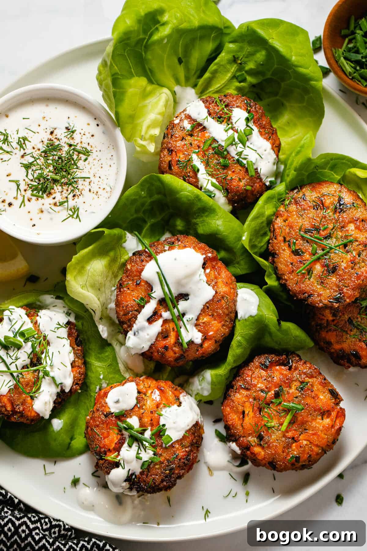 White plate with salmon patties wrapped in lettuce drizzled with tzatziki