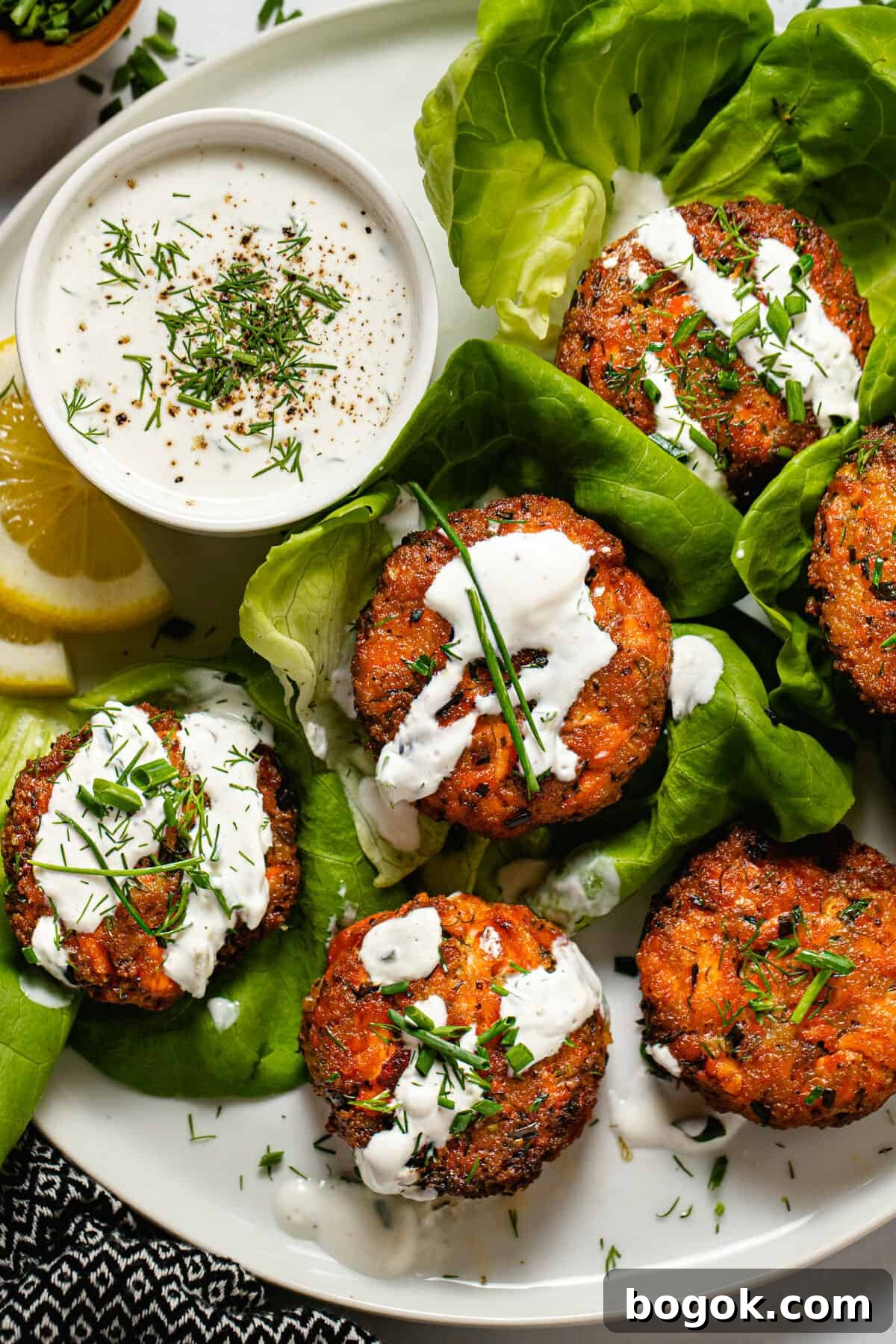 White plate with salmon patties wrapped in lettuce drizzled with tzatziki