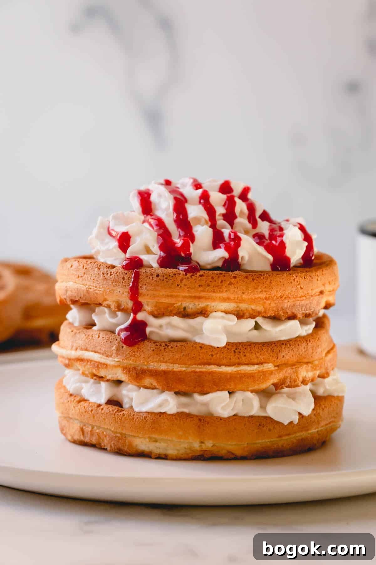 a stack of waffles with whipped cream and raspberry sauce.