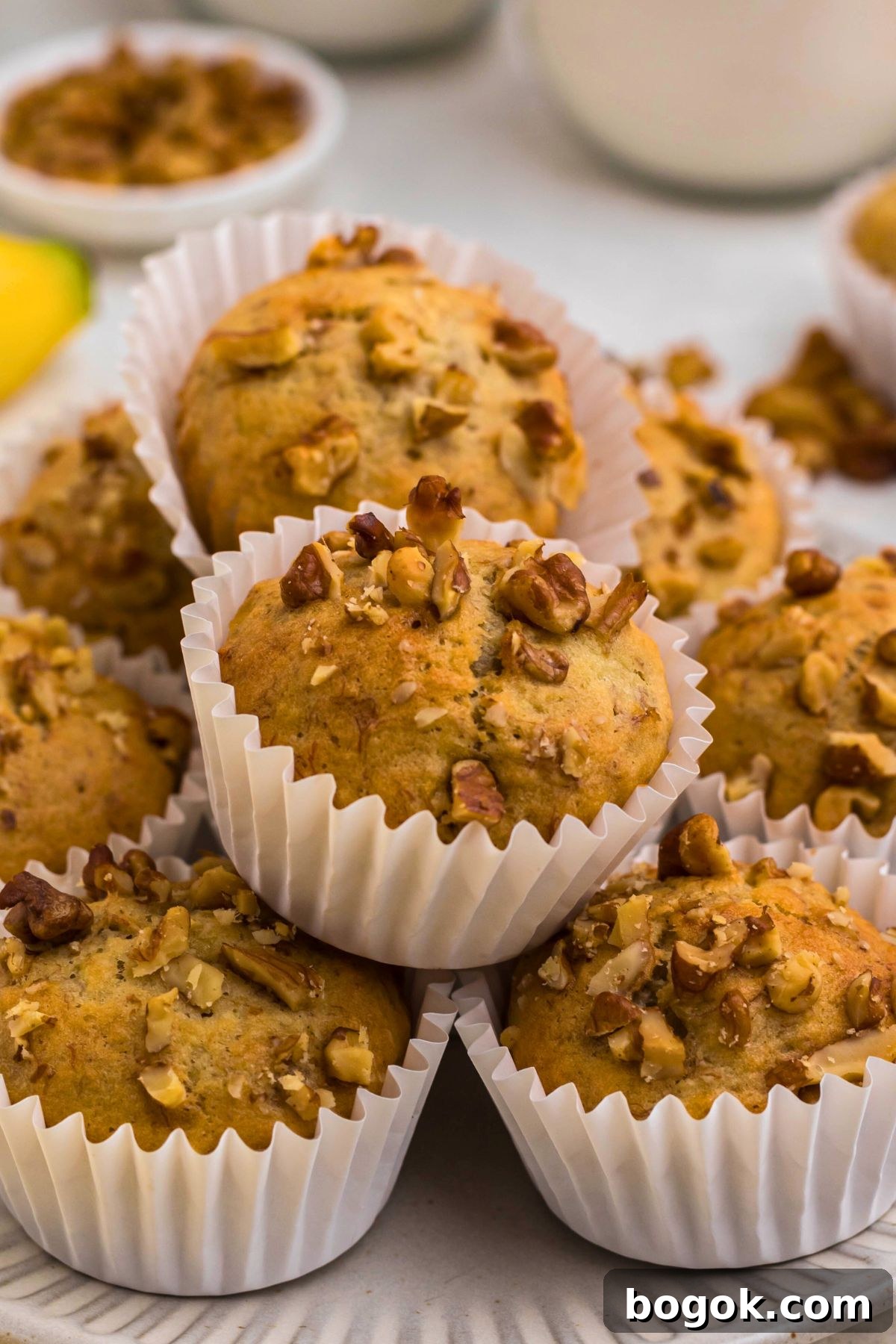 Banana Bread Muffins with Cinnamon Streusel 2 Light golden brown banana bread muffins in white liners, topped with chopped pecans.