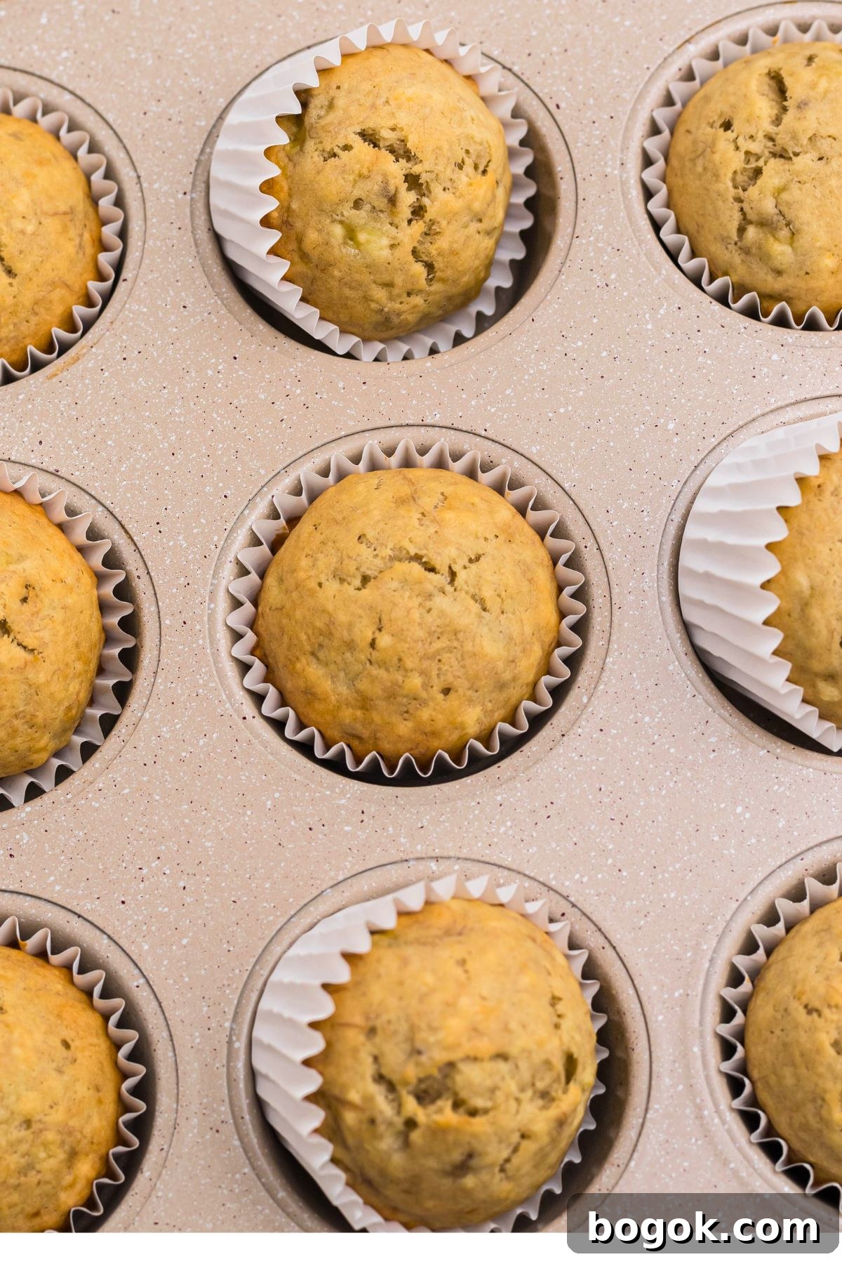 Banana Bread Muffins with Cinnamon Streusel 9 Baked muffins in a muffin pan on a marble table.