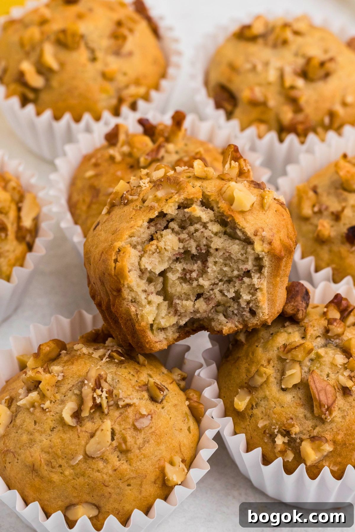 Banana Bread Muffins with Cinnamon Streusel 10 Light golden brown banana bread muffins in white liners, topped with chopped pecans.