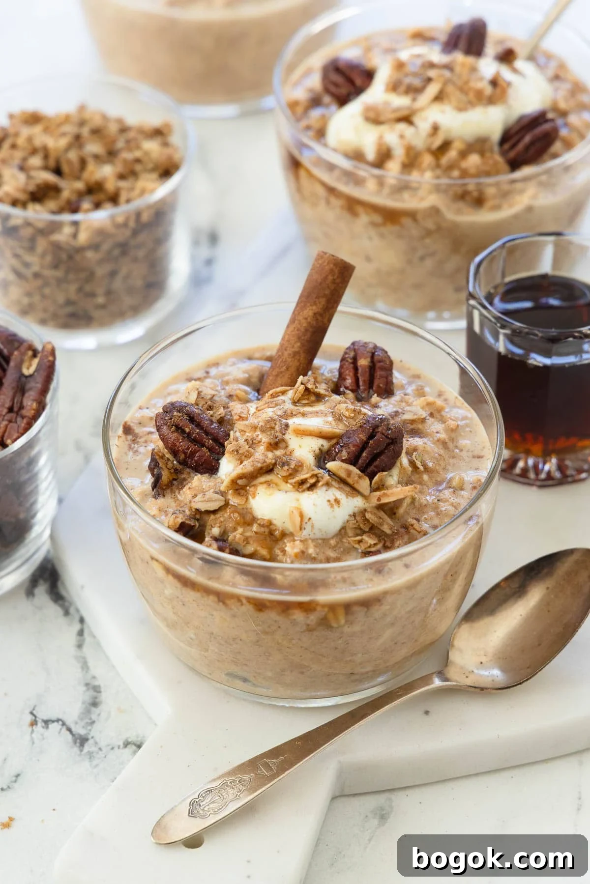 Pumpkin Overnight Oats Ready in 5 Minutes 2 Bowls of pumpkin overnight ots with cinnamon stick, pecans, yogurt, and a silver spoon.