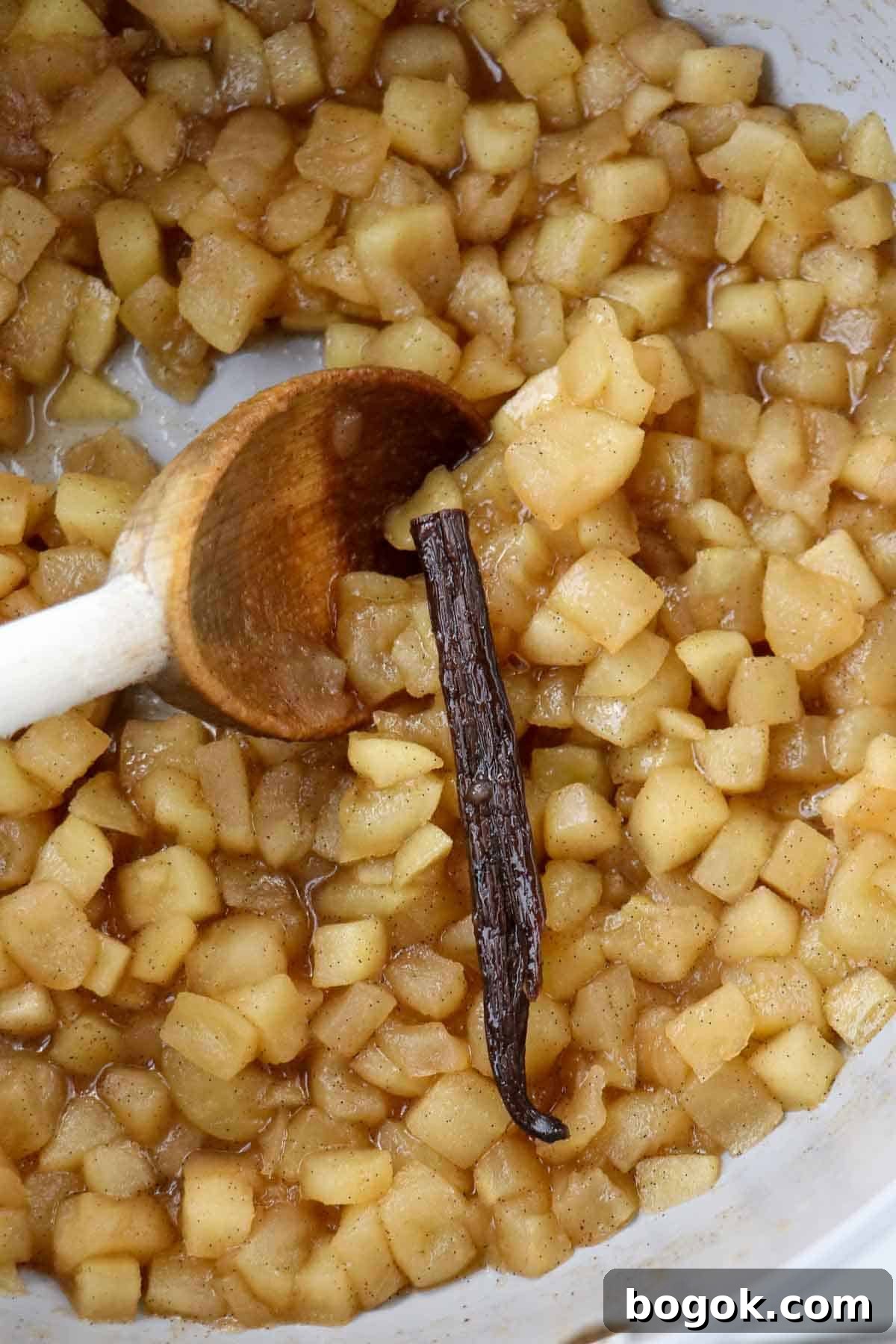 Homemade Apple Compote Recipe 6 Apple compote and a vanilla bean in a saucepan with a wooden spoon.