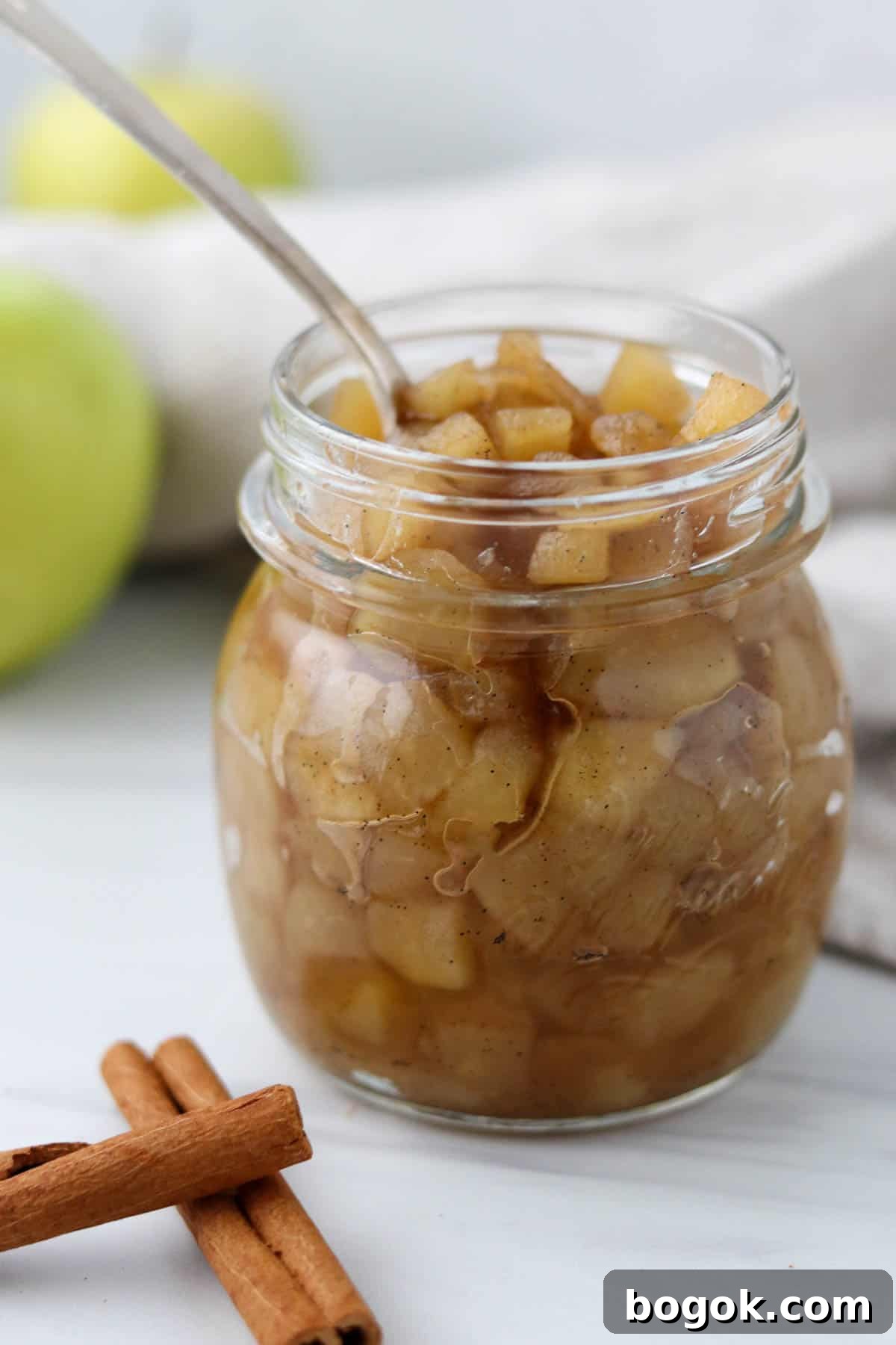 Homemade Apple Compote Recipe 7 Jar of apple compote with a spoon in it next to cinnamon sticks.