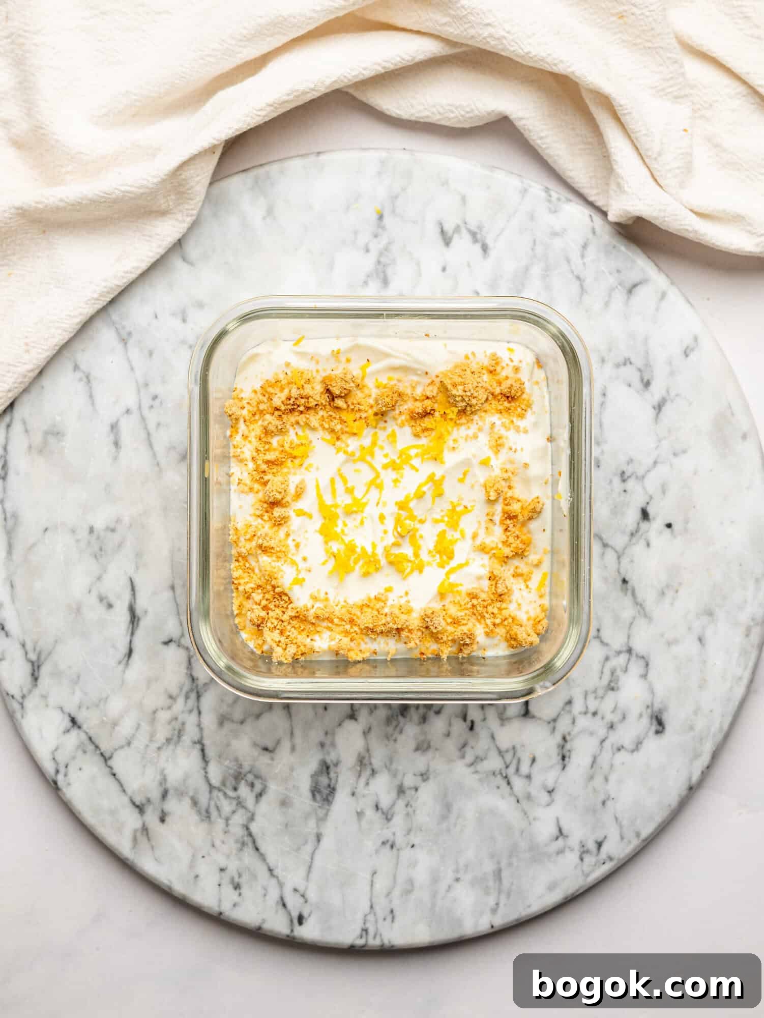 Lemon Cheesecake Overnight Weet-Bix Recipe 11 Overhead view of lemon cheesecake overnight Weet-Bix topped with biscuit crumbs and lemon zest, presented on a marble board with a draped cloth background.