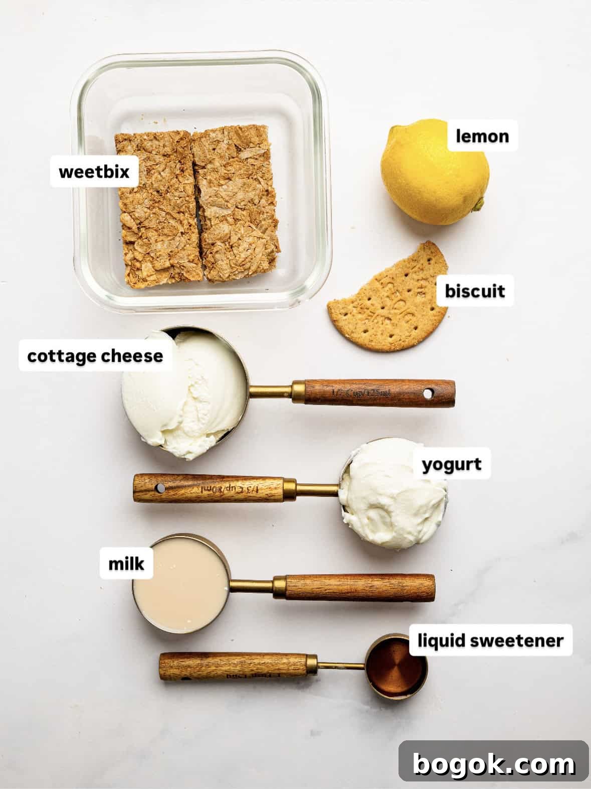 Lemon Cheesecake Overnight Weet-Bix Recipe 4 Ingredients for lemon cheesecake overnight Weet-Bix arranged on a white surface, including Weet-Bix biscuits, cottage cheese, Greek yogurt, milk, liquid sweetener, a lemon, and a biscuit for topping.