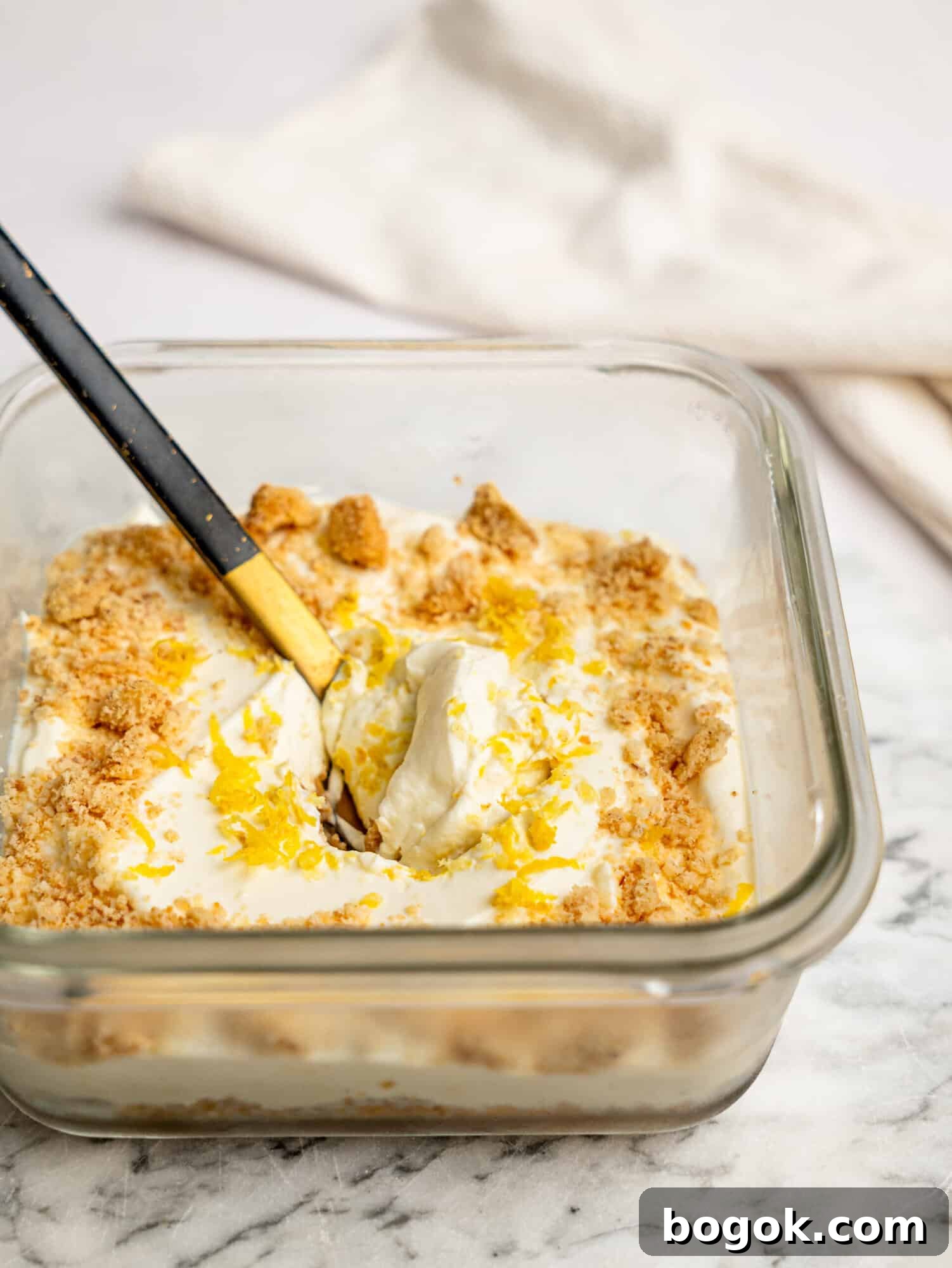 Lemon Cheesecake Overnight Weet-Bix Recipe 5 Side view of lemon cheesecake overnight Weet-Bix showing layers of Weet-Bix base and creamy lemon cheesecake filling, topped with biscuit crumbs and lemon zest.