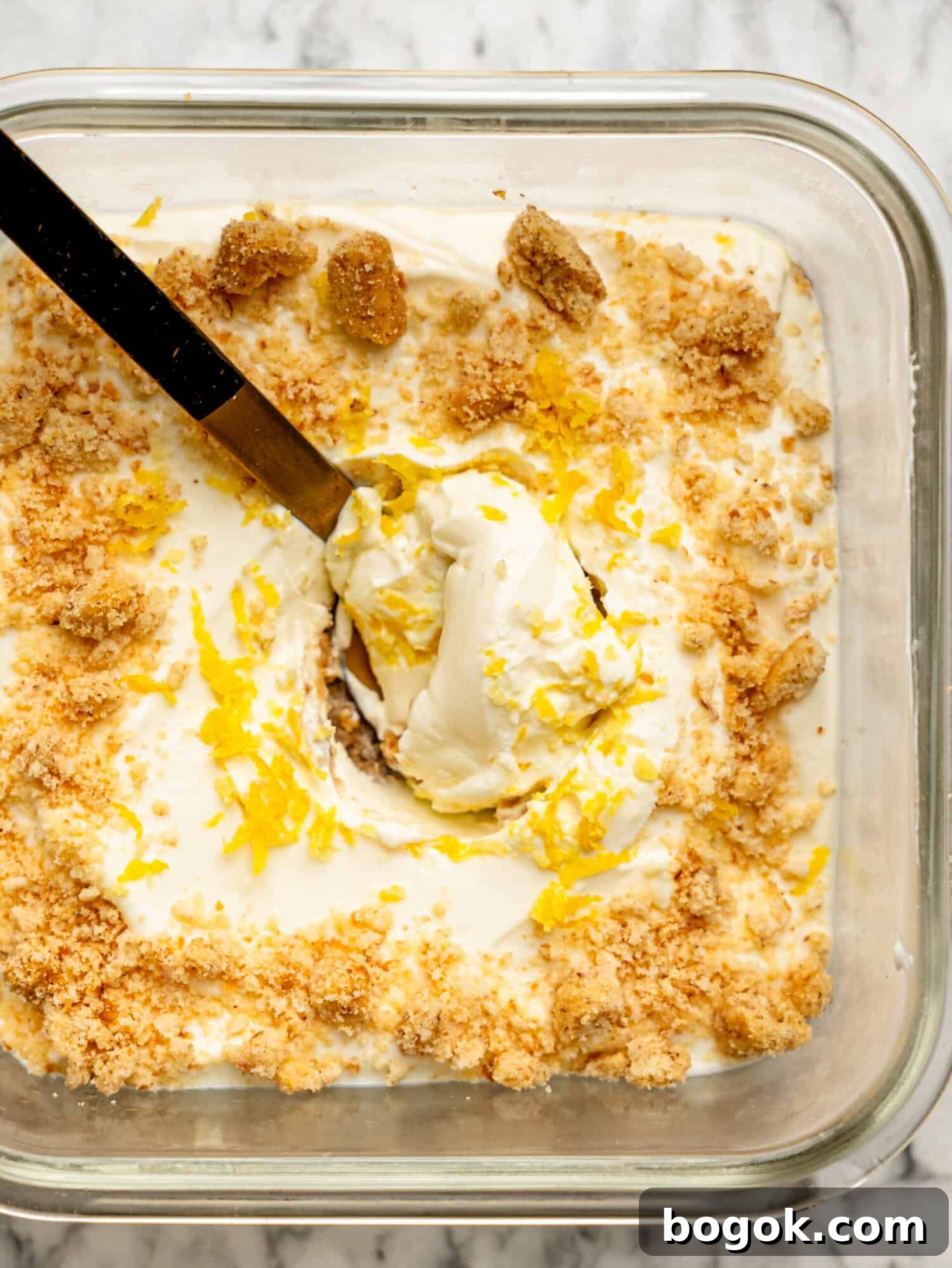Lemon Cheesecake Overnight Weet-Bix Recipe 6 Close-up overhead view of lemon cheesecake overnight Weet-Bix with a spoon lifting the creamy lemon cheesecake layer, finished with biscuit crumbs and lemon zest.