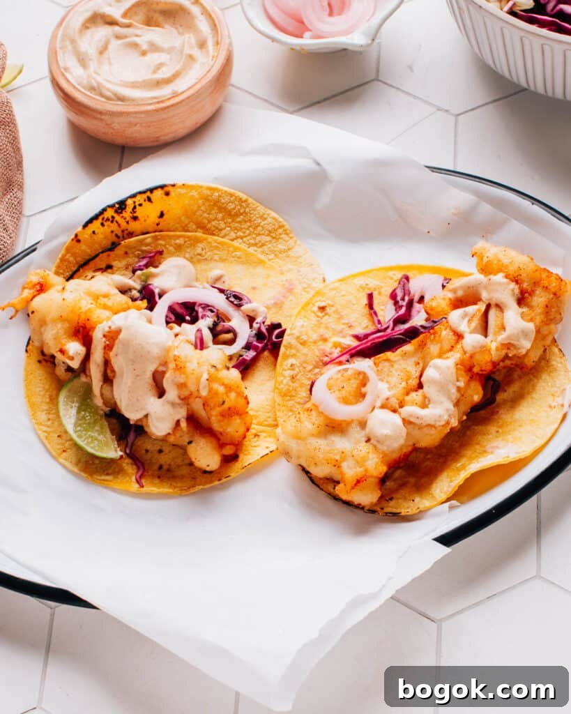 Homemade Creamy Baja Sauce for Fish Tacos 3 Two delicious Baja fish tacos artfully presented on parchment paper, drizzled with flavorful Baja sauce and accompanied by a bed of crispy cabbage slaw.