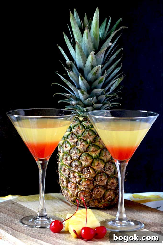 Bikini Martini Recipe: Pineapple Vodka Cocktail 4 2 martini glasses with tropical Bikini martini, pineapple and maraschino cherries on a wooden board.
