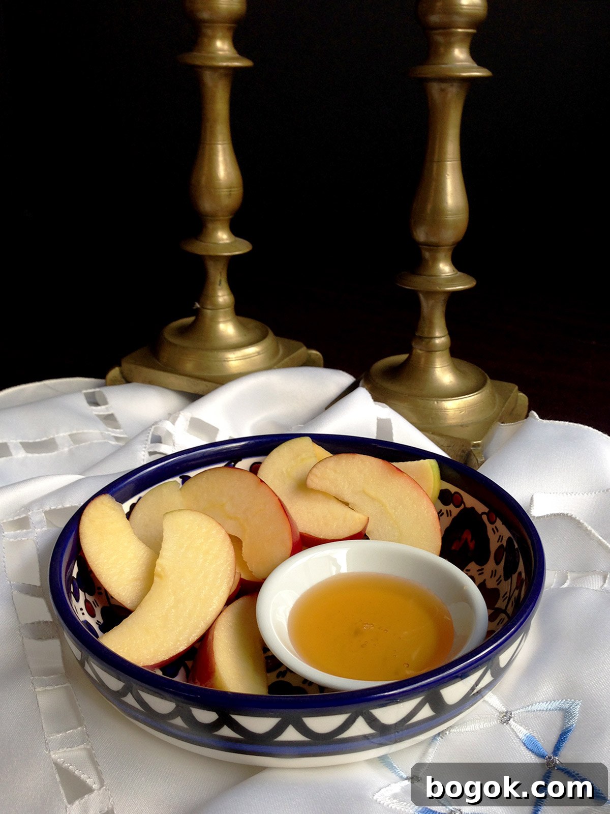 Last-Minute Rosh Hashanah Prep Guide 2 Apples and honey in a blue bowl with two shabbat candlesticks in the background.