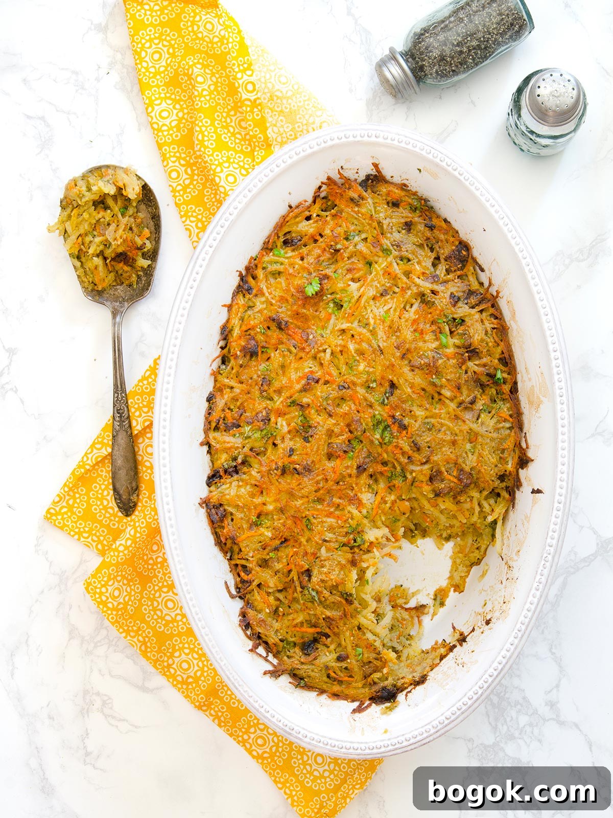 Last-Minute Rosh Hashanah Prep Guide 23 Top down view of a whole oval white pan of potato kugel with a spoon of it on the side.