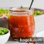 A jar of homemade sweet chili vinaigrette dressing with a spoon sticking out of it and a salad behind it.