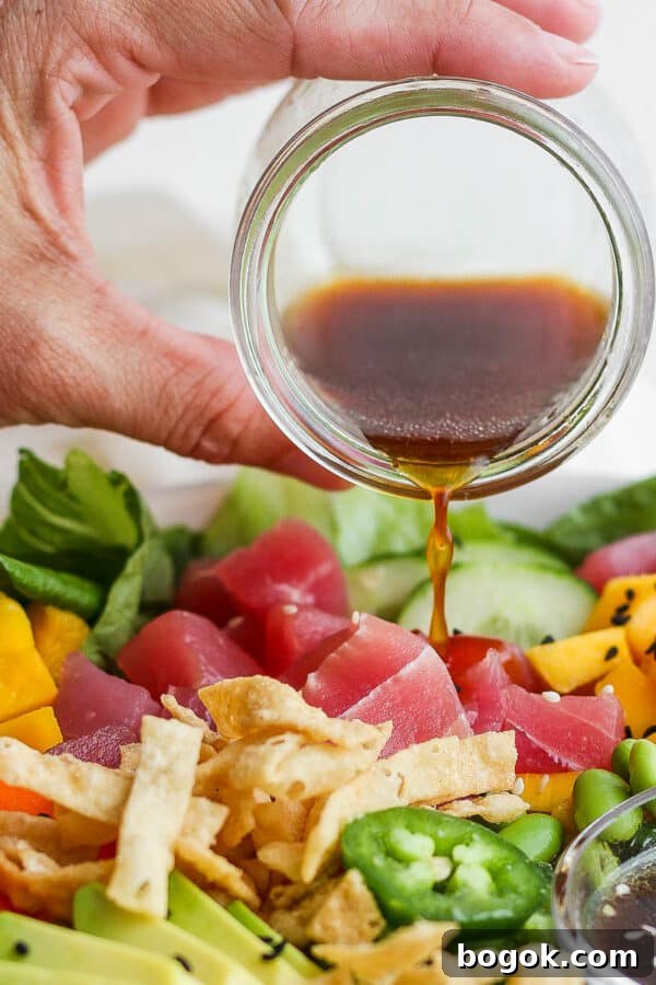 Someone pouring homemade sesame ginger dressing over a poke salad with tuna, mango and avocado.